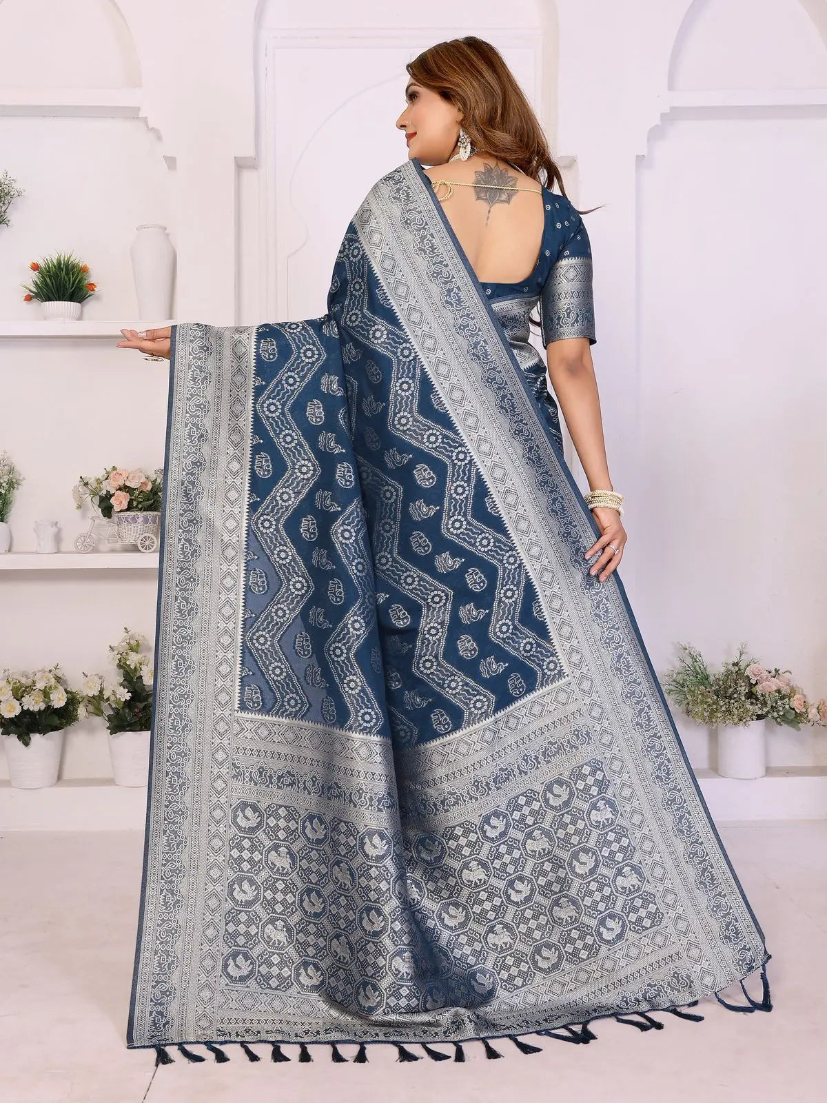 Woman wearing a blue saree with a white pattern in a bright room.